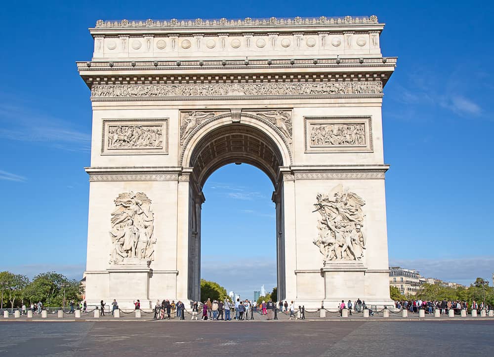 Famous Arc de Triomphe in Paris on a sunny day with many tourist in front.