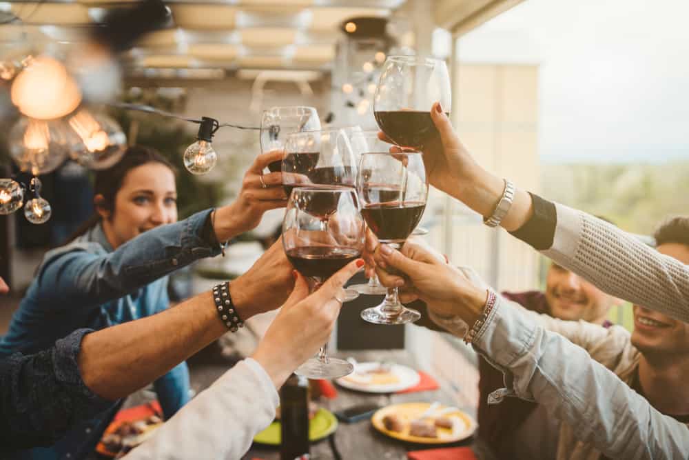 A group of people at a dinner party raising their glasses of red wine.