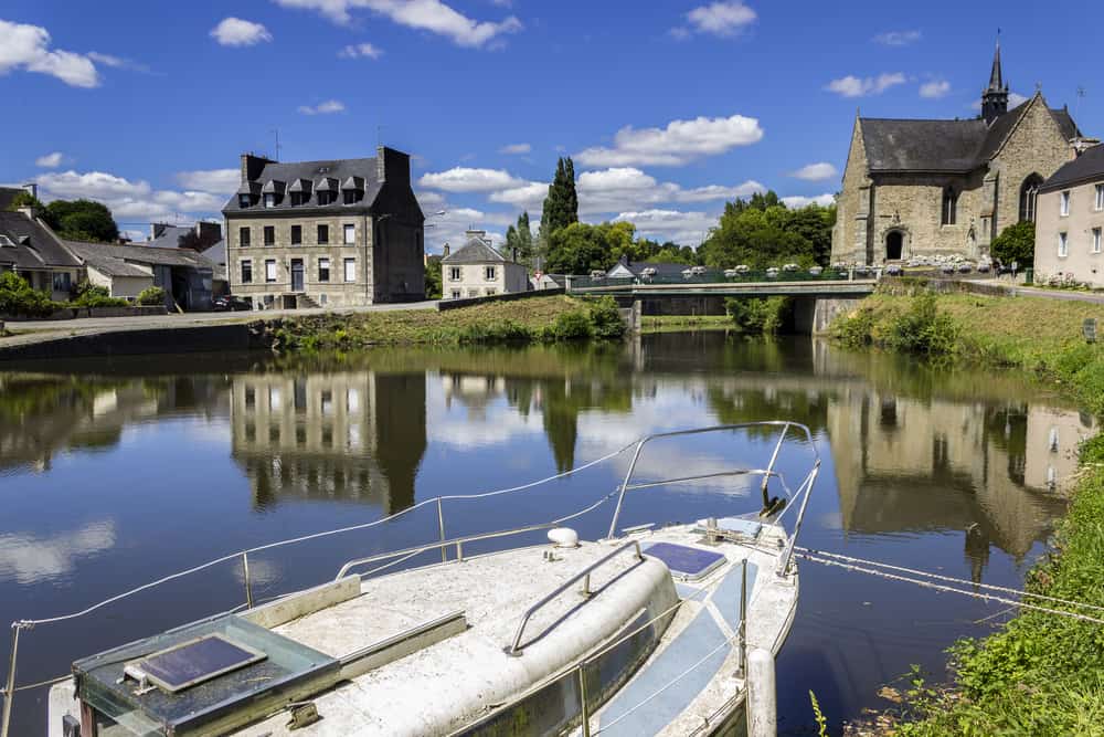 A view at Brest in Brittany, France from the Canal de Nates. A boat and the river in the foreground and old buildings and a bridge in the back.