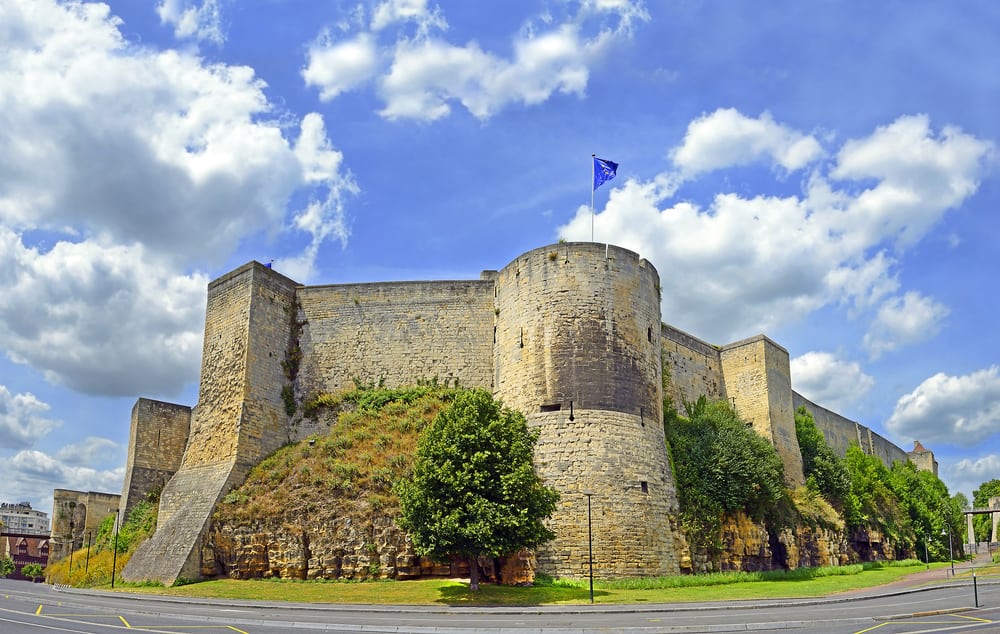 Outside view of the majestic Castle of Caen in Normandy, France. Bright day with blue sky and a flag in one of the towers.