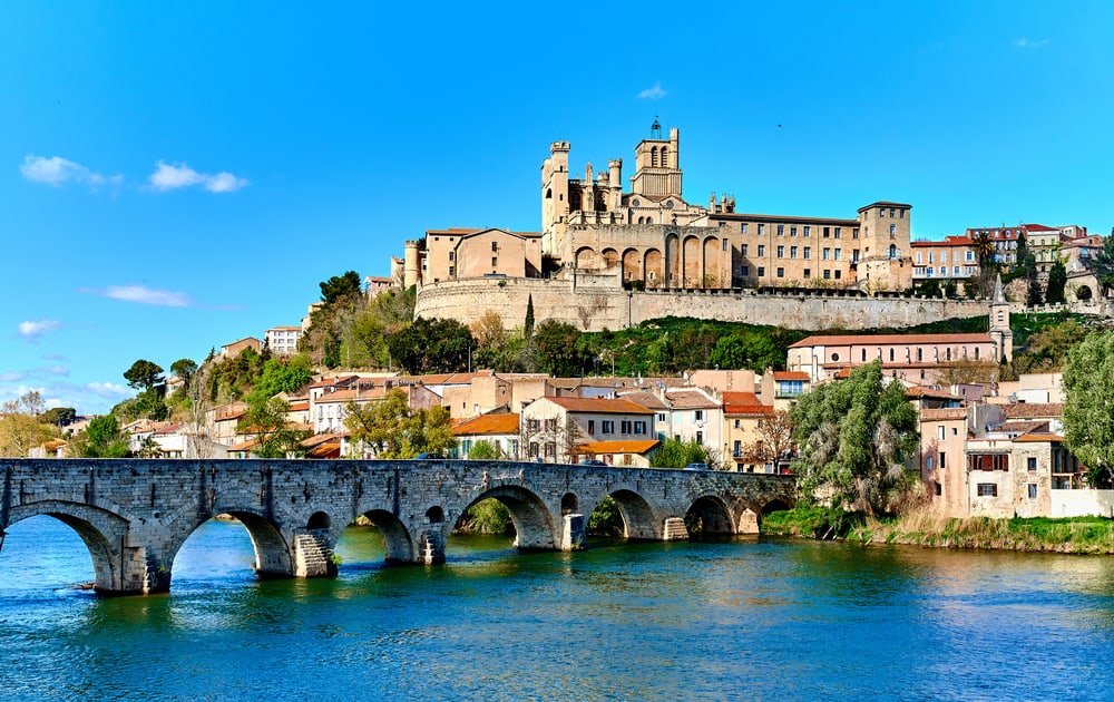A view from the river of Cathedral Saint-Nazaire in Beziers, France. In the front an old bridge crossing the river.