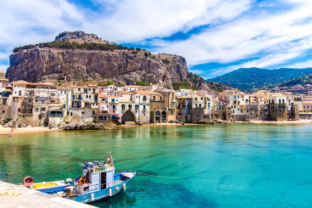 Panorama view of Cefalu on Sicily, Italy. Small boat in the front and mountains in the background.