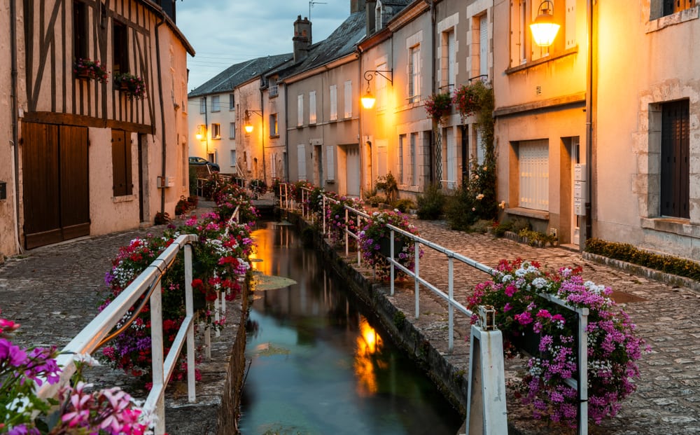 A beautiful evening in Beaugency. A fence above a small creek decorated with flowers and old house at both sides.