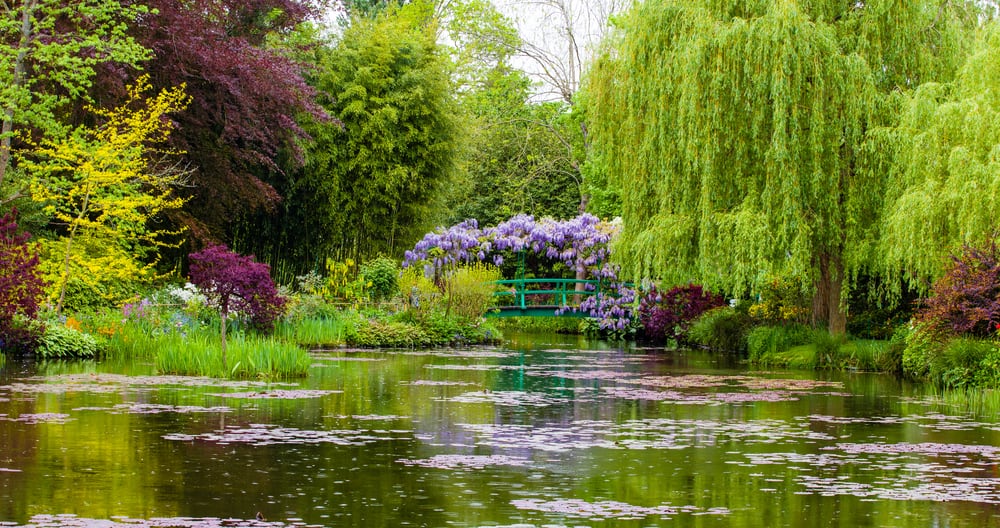 Garden in the town of Giverny in France with a little lake, trees, plants, and a bridge.