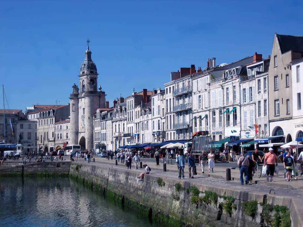 Busy street with many people and old houses is La Rochelle, France.
