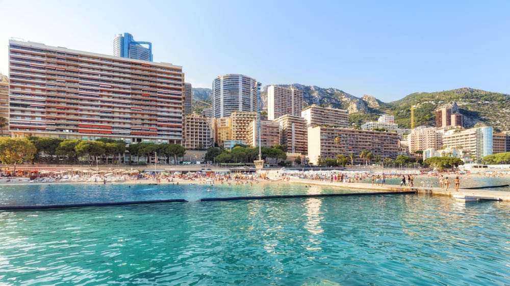 Fantastic view of Larvotto Beach in Monte Carlo, Monaco. Clear blue water and large hotel buildings in the back.