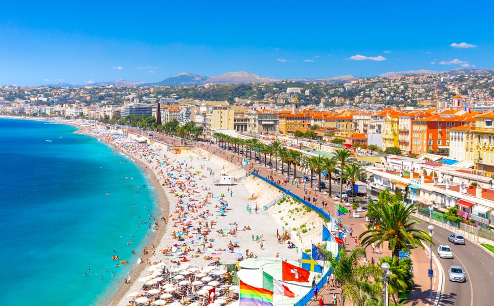 Aerial view of Promenade des Anglais in Nice on a sunny day. Palm trees, beach, ocean, and colorful buildings.