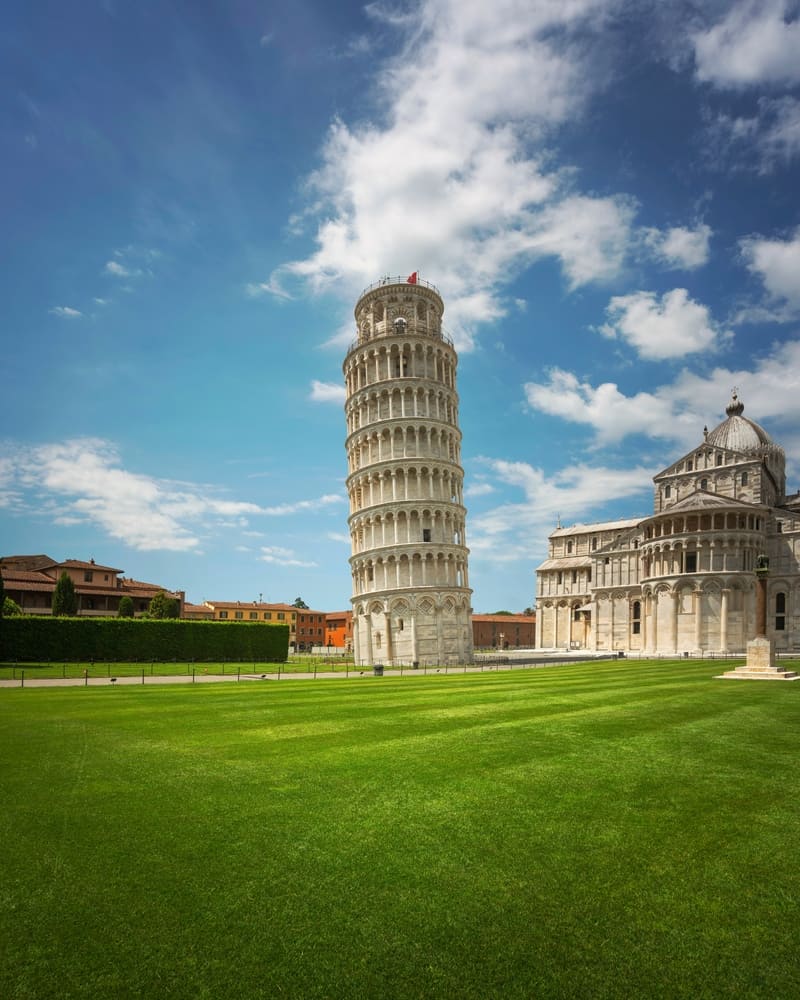 The Leaning Tower of Pisa. Clear blue sky. Green field. Old buildings.