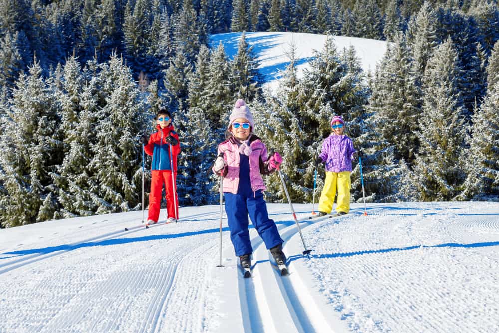 Three children skiing in Megeve in the French Alps. Lots of snow and trees in the background.