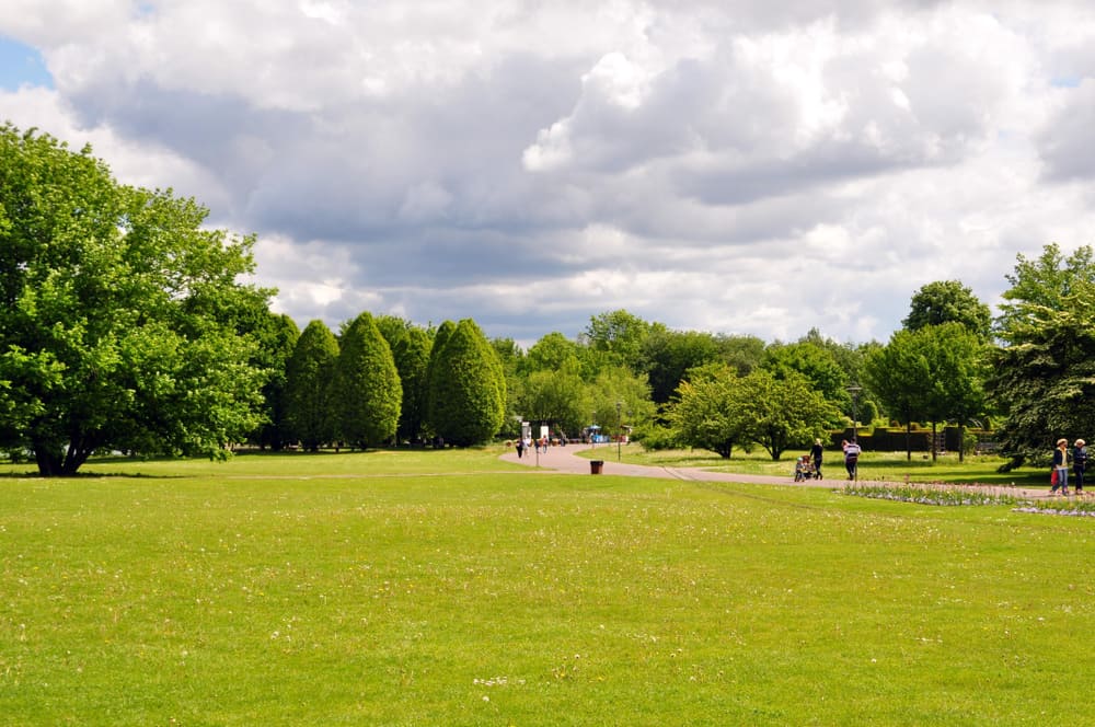 A large open area with a lawn in Britzer Garten. People strolling on a path way.