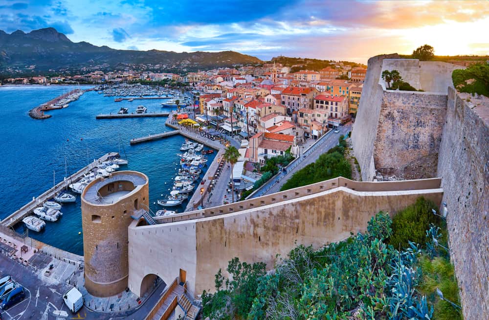 Walls of the citadel of Calvi on the old town with historic buildings at evening sunset. Bay with yachts and boats. Luxurious marina and very popular tourist destination. Corsica, France