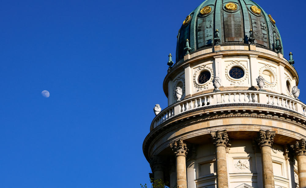 Close up of the dome of the Französischer Dom in Berlin. Copper with gold inserts on the background of a clean, blue sky with a large moon.