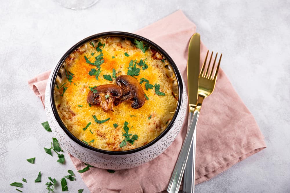 Julienne with potatoes and mushrooms in a baking dish on a light background. Traditional French dish.