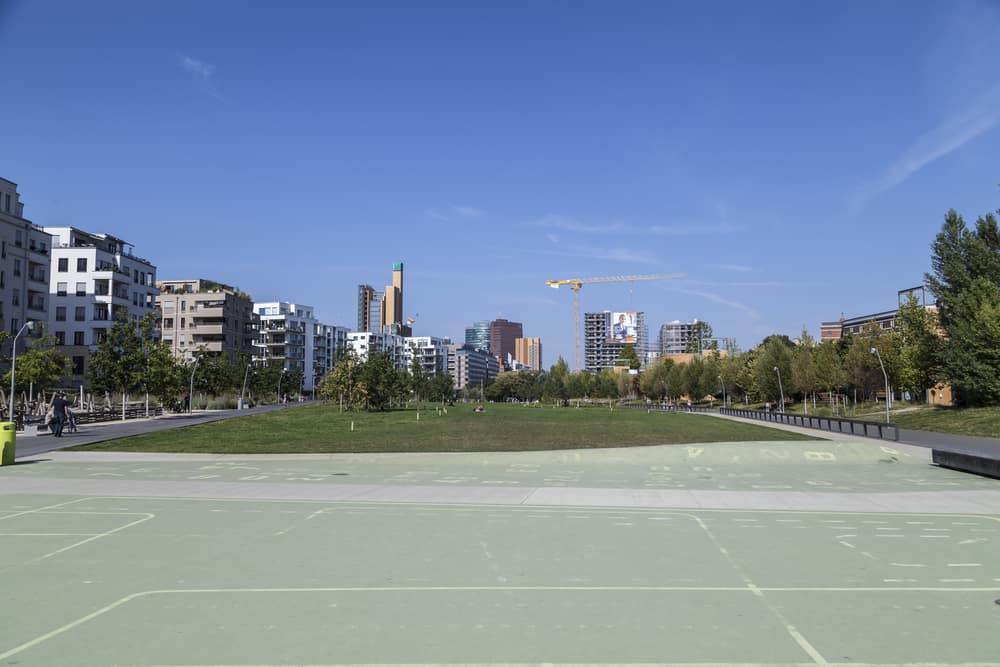 Panoramic view of Park at Gleisdreieck in Berlin, Germany. Large field surrounded by trees and tall buildings in the back.