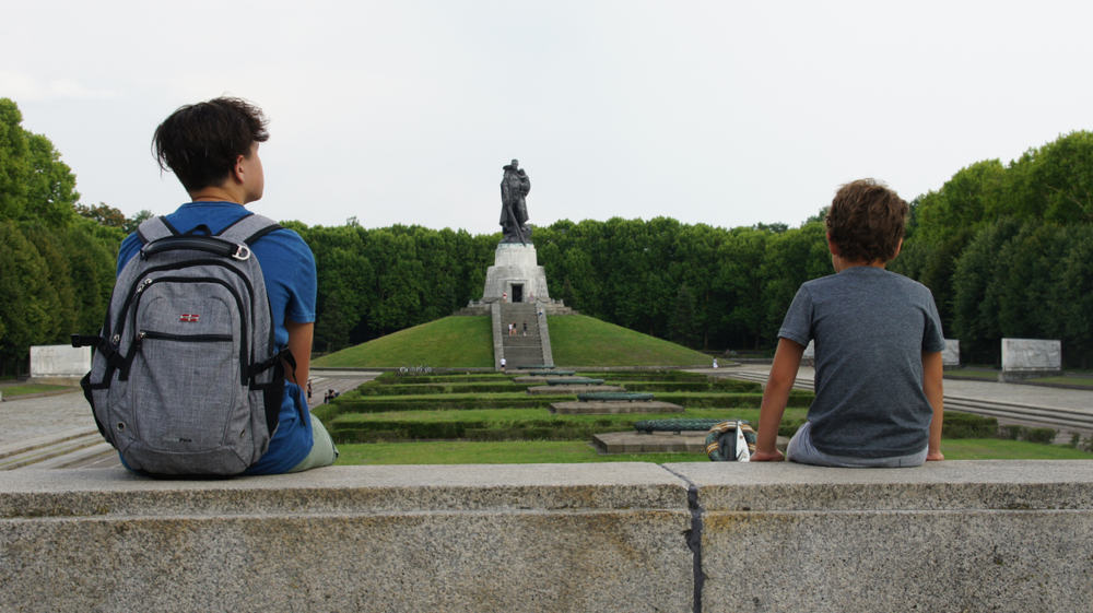 Two boys sitting and watching a statue in Treptower Park in Berlin, Germany.