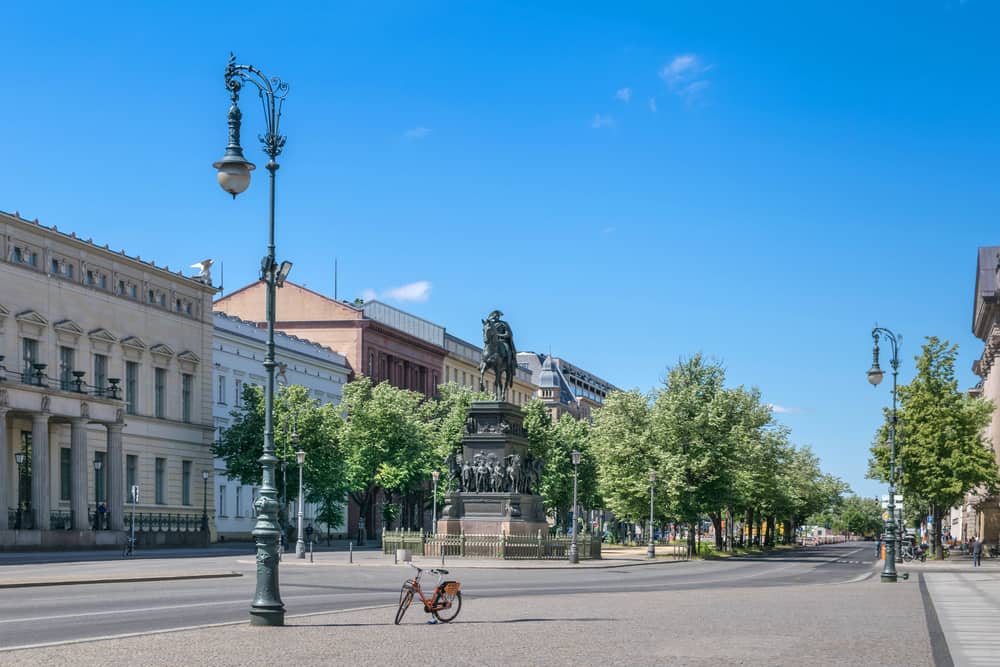 A view down an empty Unter den Linden boulevard in the central Mitte district of Berlin. Statue of King Frederick II of Prussia and linden trees.