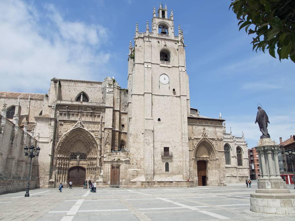 Outside view of Cathedral of Palencia in Spain. A few people and a statue in front.