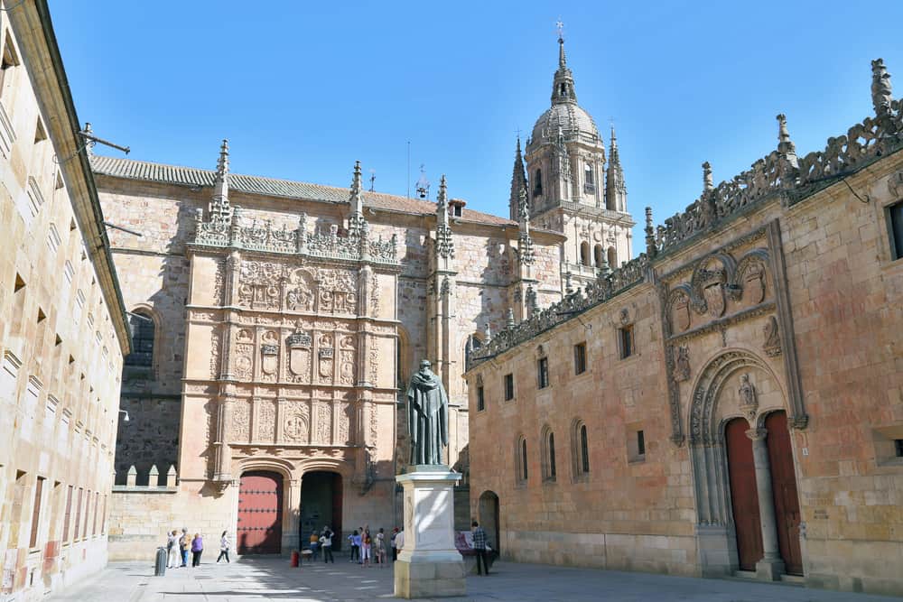 Outside view of the University of Salamanca. People and a statue in front.