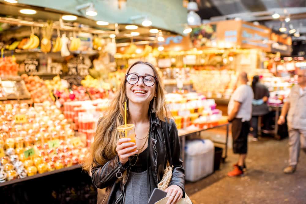 Young smiling woman drinking orange juice at the famous food market La Boqueria in Barcelona, Spain.
